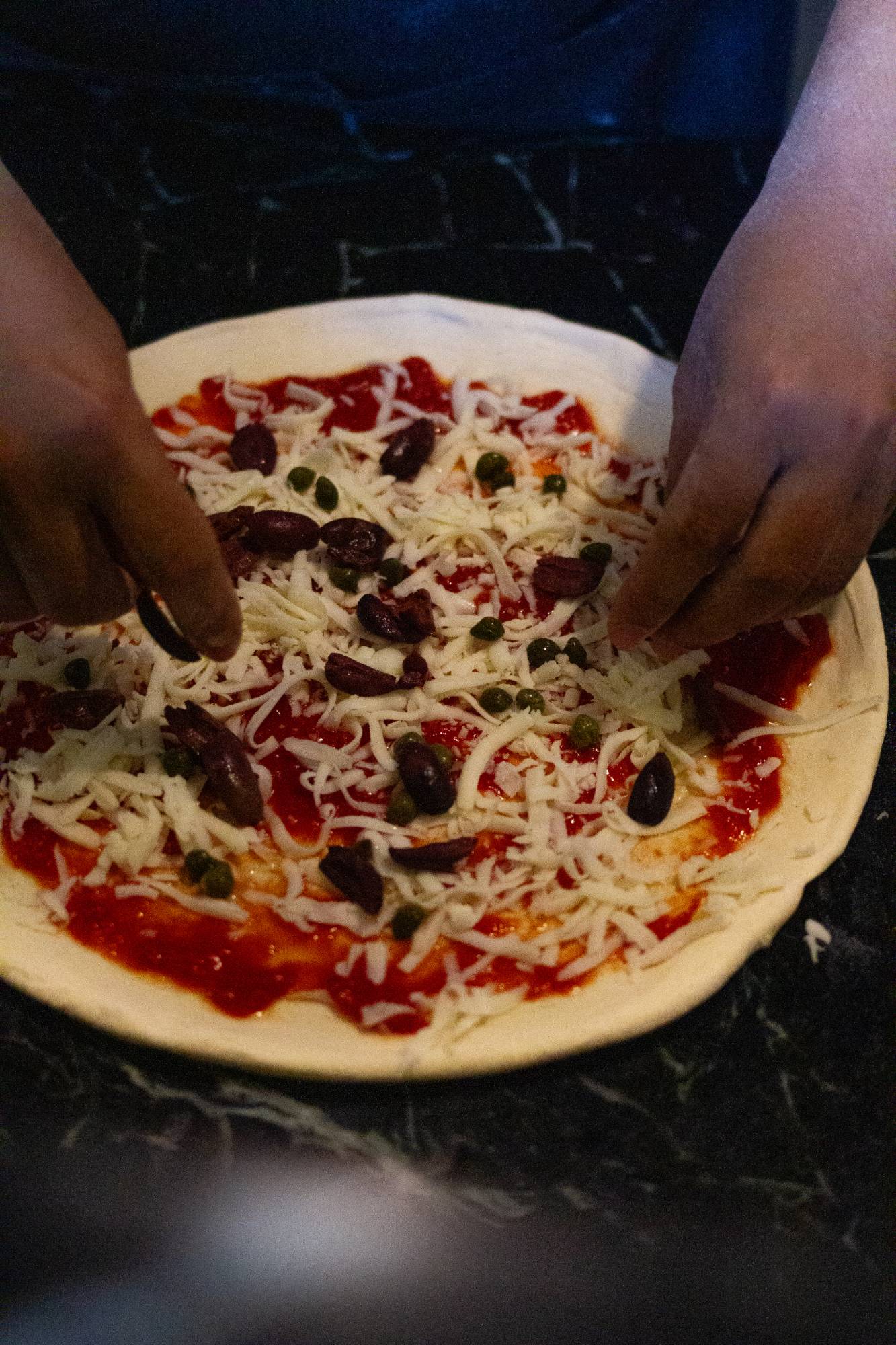 Chef's hands topping a pizza with olives and capers