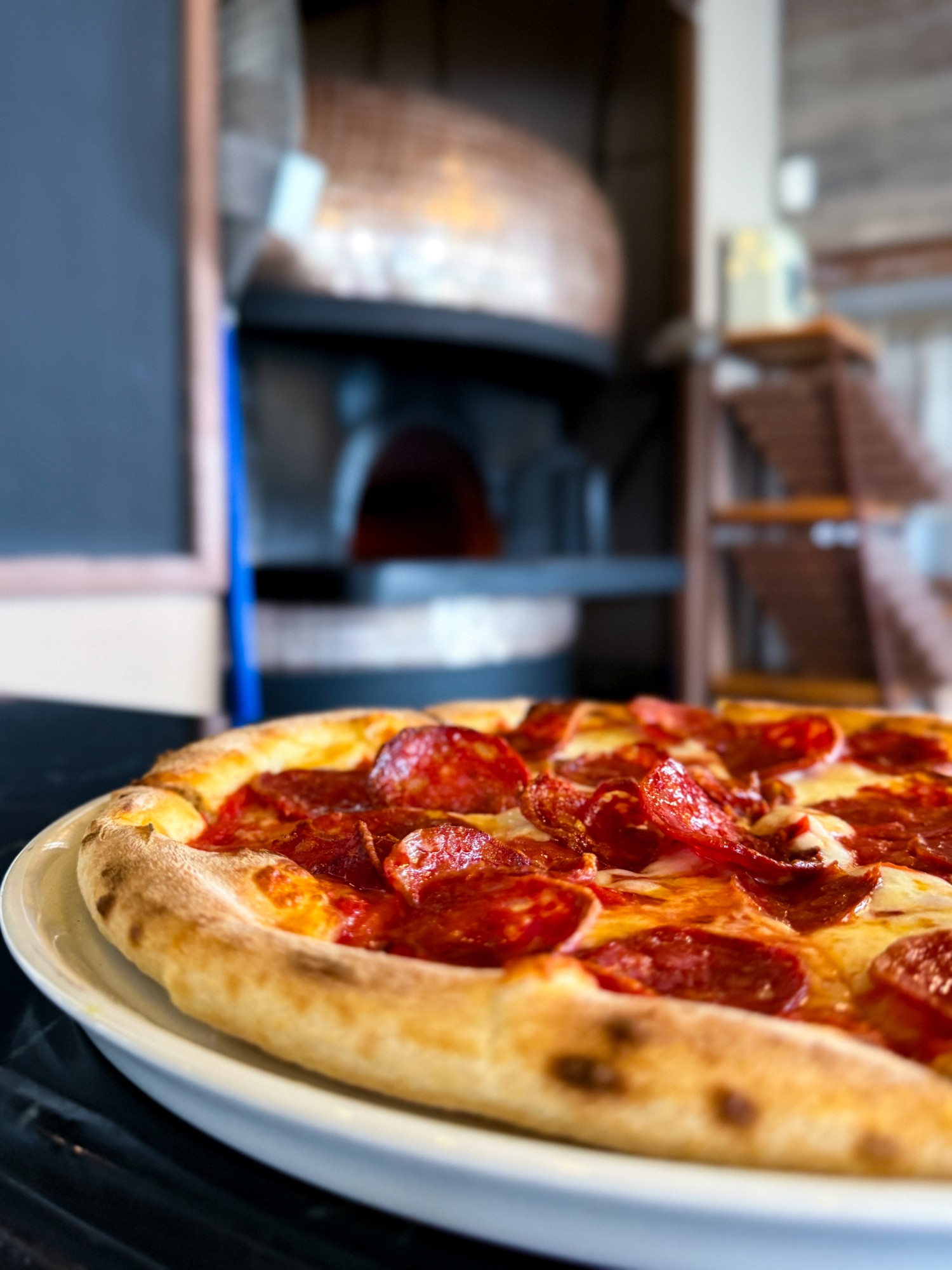Close-up of a pepperoni pizza with the oven behind