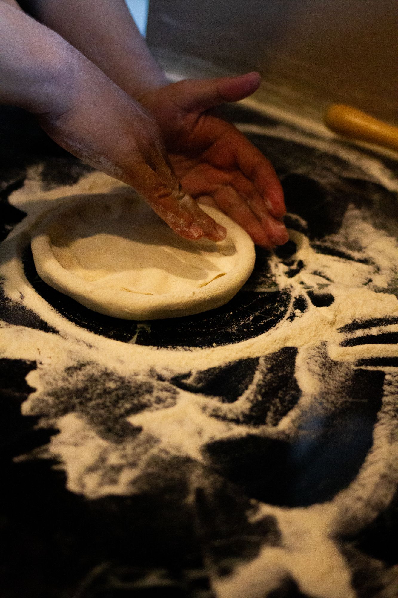 Pizza dough being pressed out on a floured counter