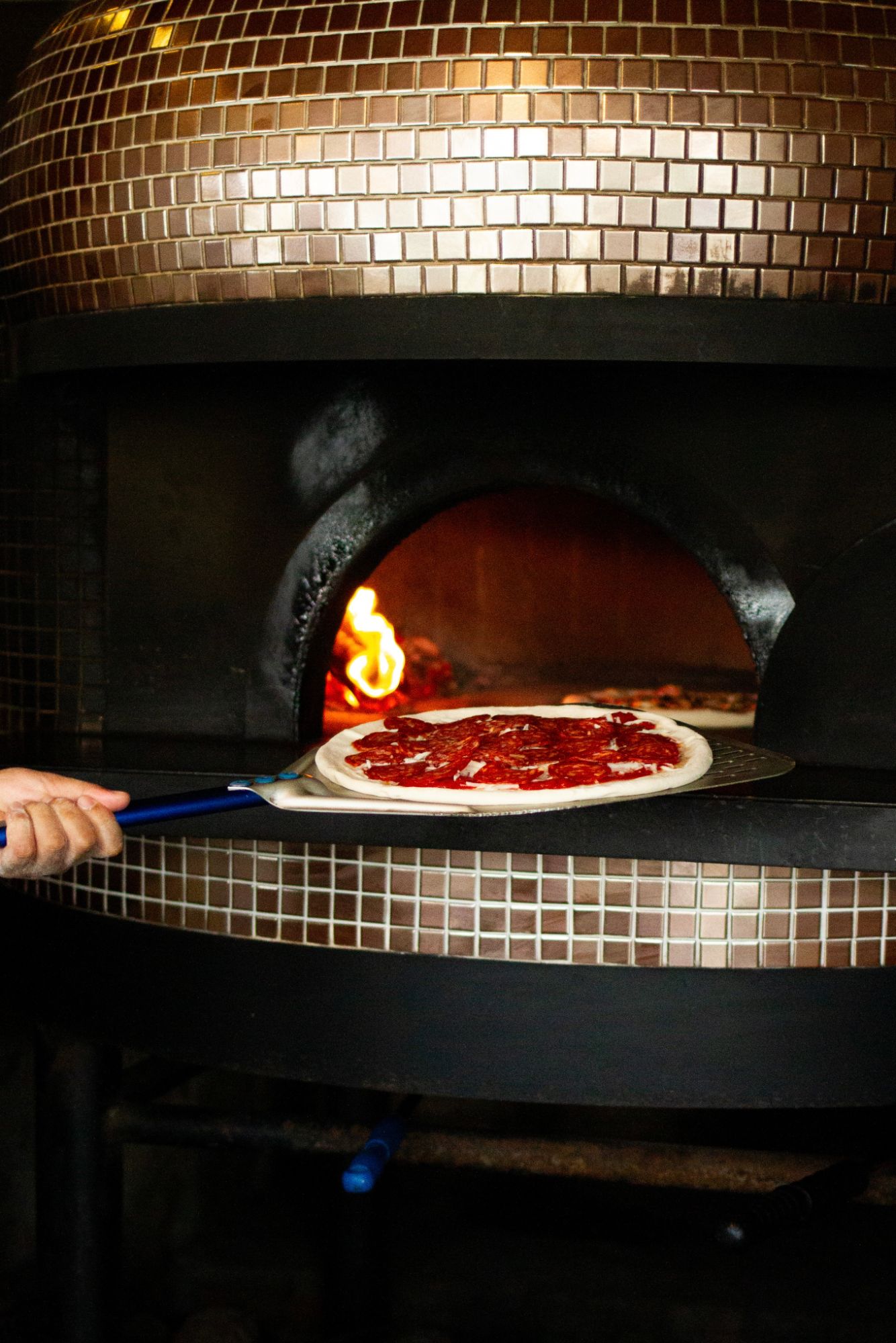 Salami pizza going into the tiled wood-fired oven