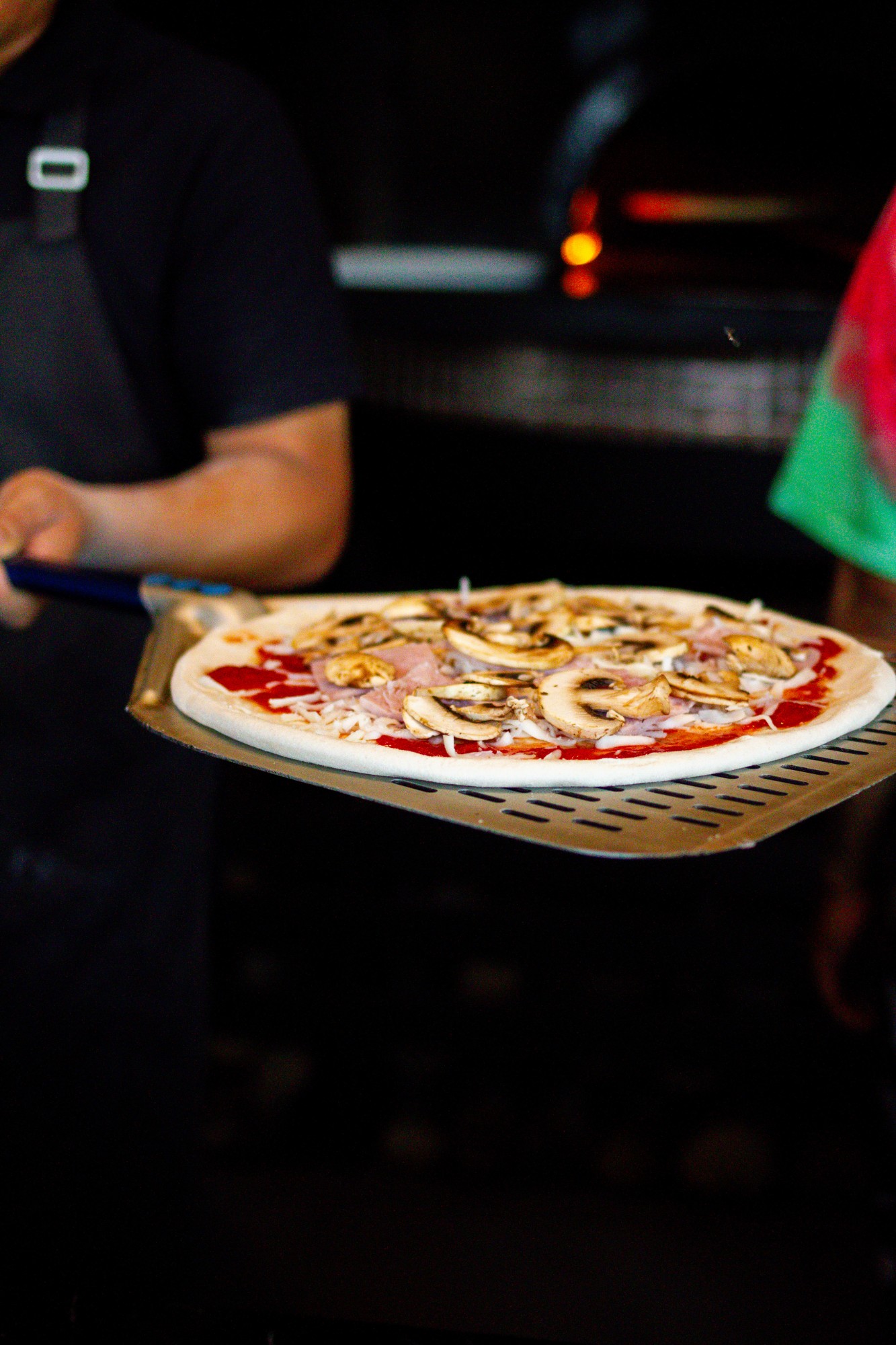 Ham and mushroom pizza on a peel heading for the oven