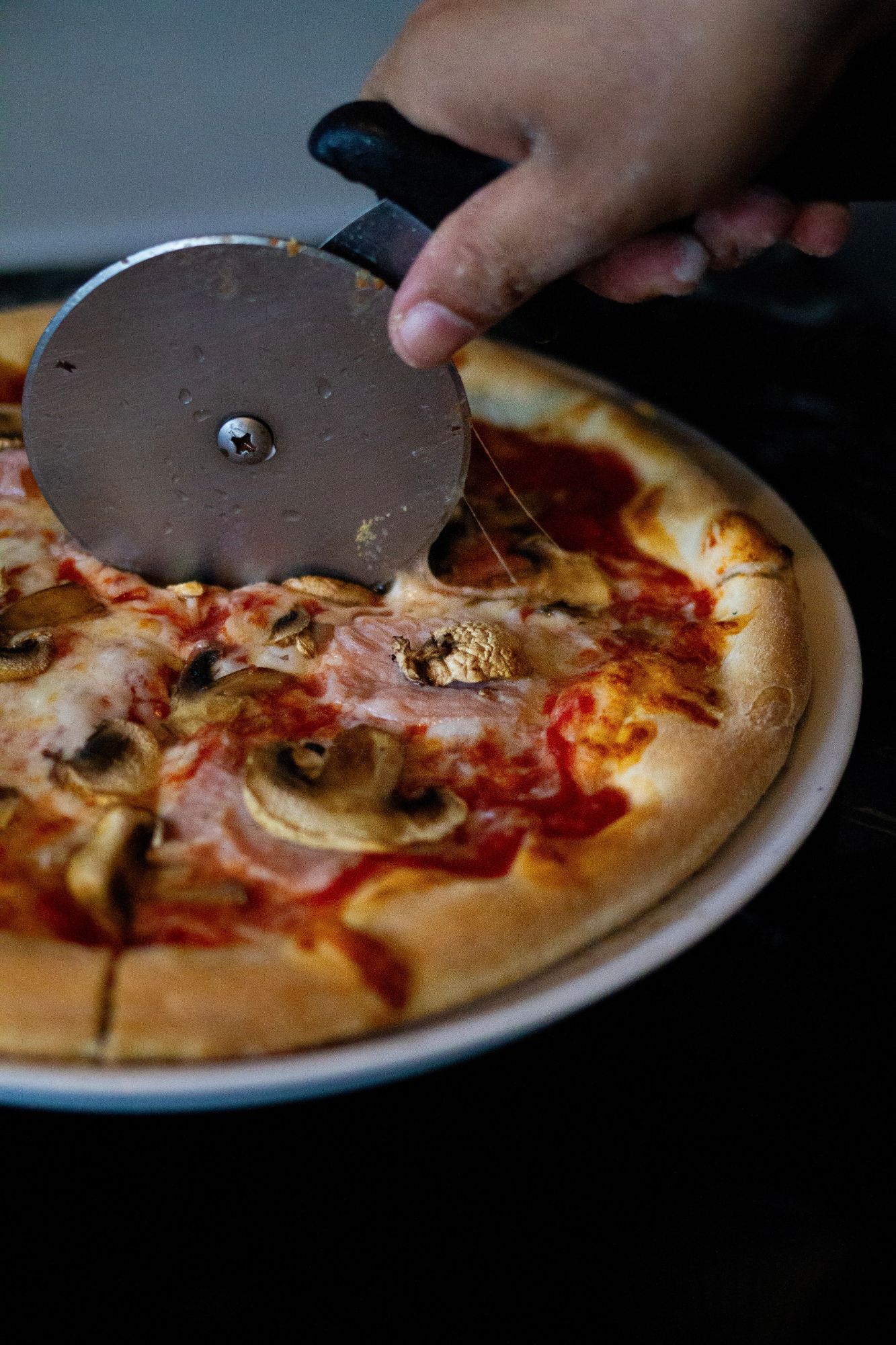 Ham and mushroom pizza being sliced with a pizza wheel
