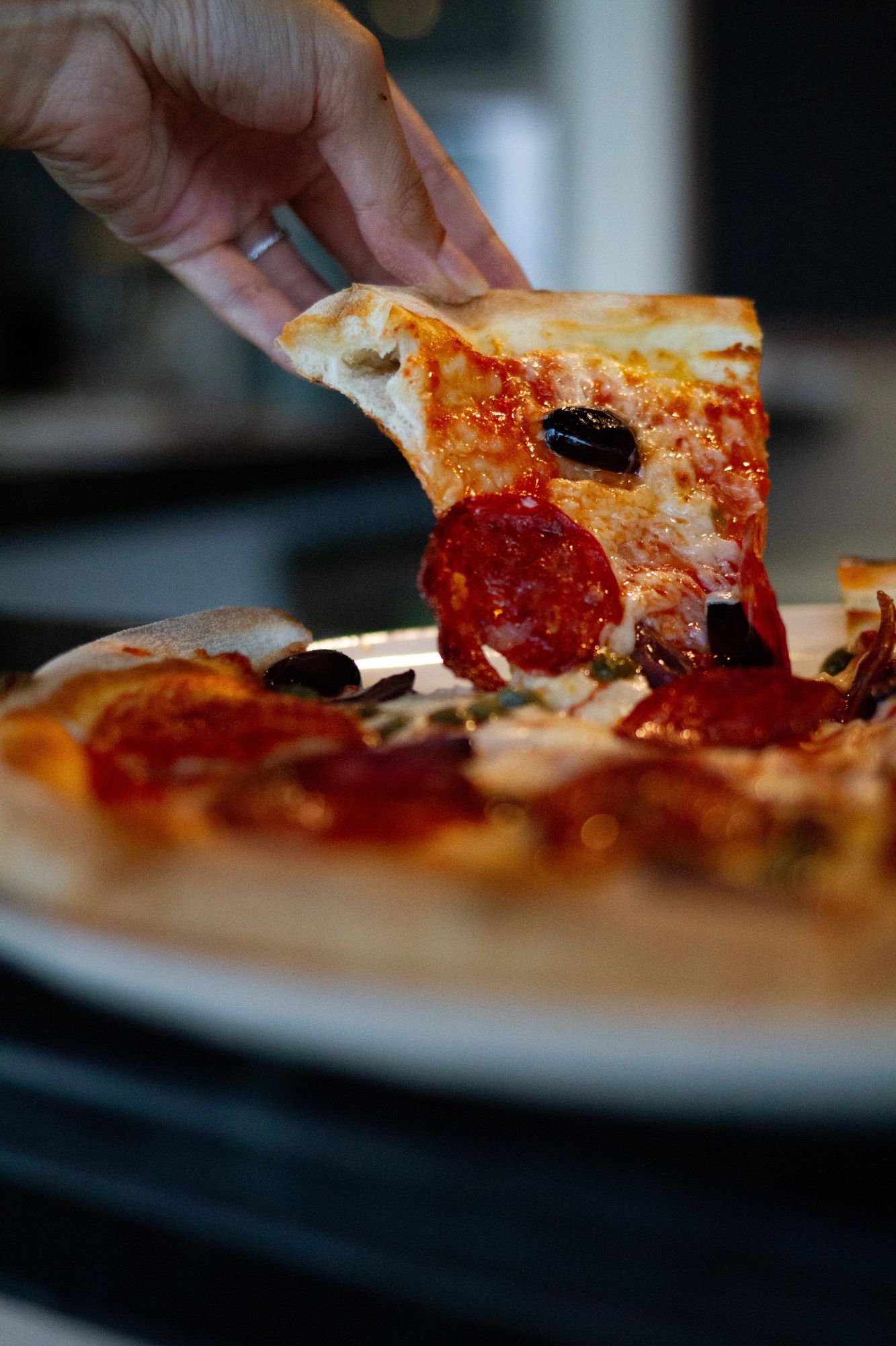 A slice of salami and olive pizza being lifted from the plate