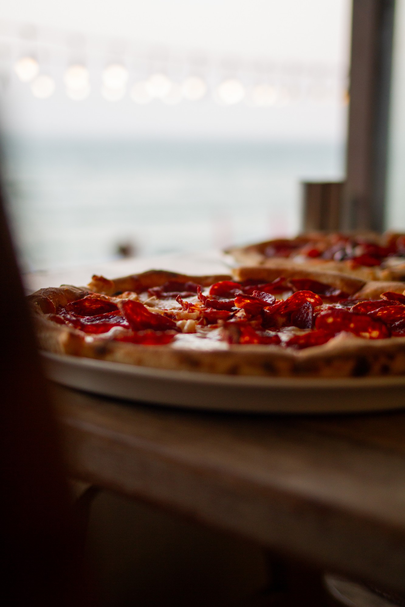 Salami pizza on a table with the sea visible behind