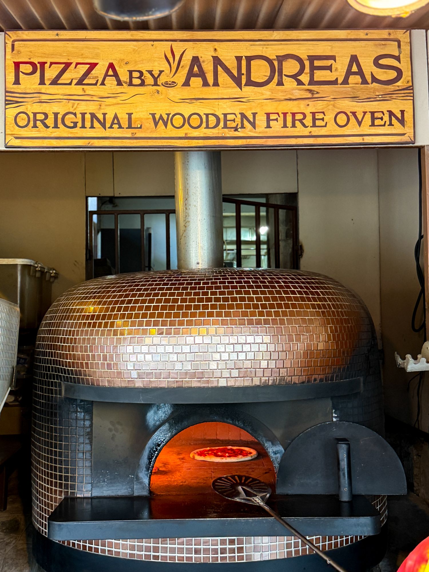 Tiled dome oven under the Pizza by Andreas sign, pizza baking inside